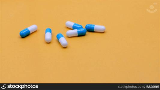 Blue-white capsules pill on yellow background. Pharmacy banner. Capsule pills manufacturing industry. Pharmaceutical industry. Drug development and new drug research concept. Capsule pills industry.