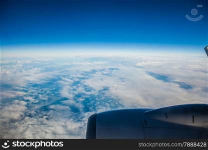 Blue white cloudy sky and engine. View from window of airplane flying in clouds. Skyscape cloudscape. Bird&#39;s eye.