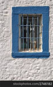 blue window with bars on white house in Greece
