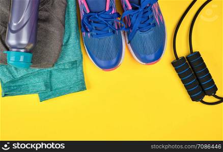 blue women&rsquo;s sneakers and clothes for sports and fitness on a yellow background, top view, copy space, flat lay