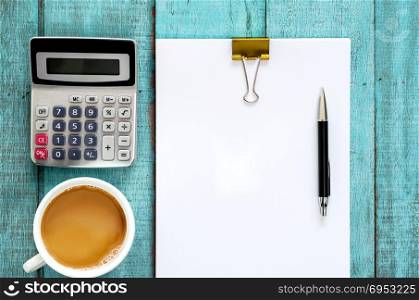 Blue wooden desk table with paper ream, pen, calculator and cup of coffee. Top view with copy space, flat lay.