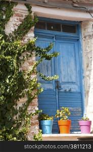 Blue wooden door and colorful flowerpots of stone house