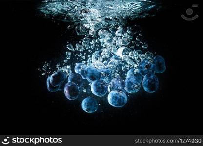 Blueberries falling into a water isolated on black background. Sinking under water with lots of air bubbles. Blueberries falling into a water isolated on black background