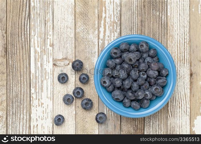 blueberries in a blue ceramic bowl on a grunge white painted wood surface
