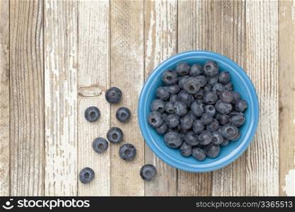 blueberries in a blue ceramic bowl on a grunge white painted wood surface
