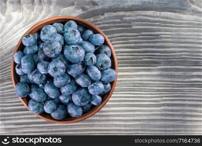 Blueberries in a brown clay bowl on a wooden background. View from above. Blueberries in brown clay bowl on wooden background