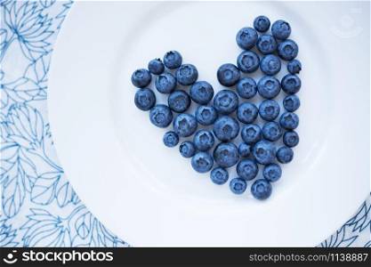 blueberries in a heart shape on a white plate. valentine card. blueberries in a heart shape on a white plate