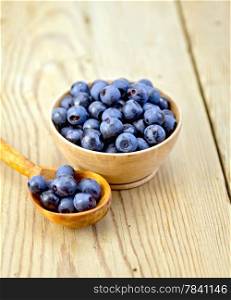Blueberries in a wooden bowl and spoon on a wooden boards background