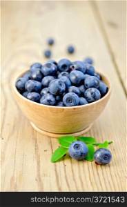 Blueberries in a wooden bowl with a sprig of green leaves on the background of wooden boards