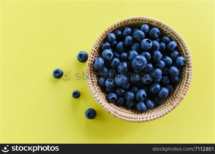 Blueberries in basket on yellow background , top view
