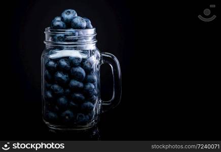 Blueberries in glass jar isolated on black background. Copy space on right.. Blueberries in glass jar isolated on black background.