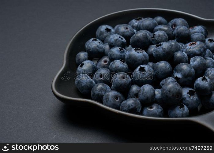 Blueberries on a black clay pan with black background, closeup view.