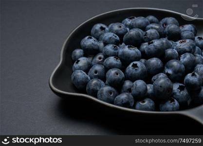 Blueberries on a black clay pan with black background, closeup view.