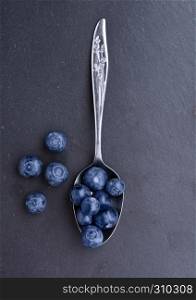 Blueberries on old spoon on black stone kitchen board. Natural healthy food. Still life photography
