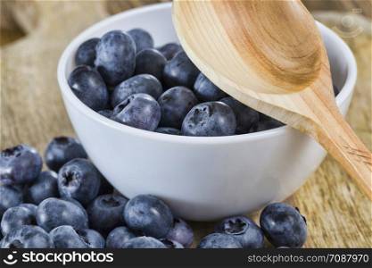 Blueberries on the table in a white bowl, summertime, photo of ripe and tasty berries close-up with a rustic wooden spoon. Blueberries on the table