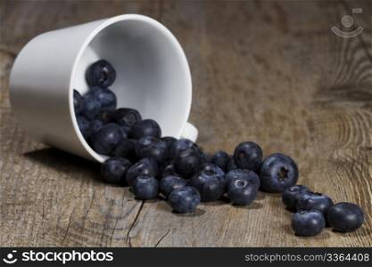 blueberries rolling from a fell over cup. blueberries rolling from a fell over cup on wooden background
