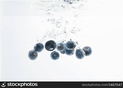 Blueberries sinking underwater with air bubbles isolated on white background. Berry fruit theme.. Blueberries sinking underwater with air bubbles isolated on white background