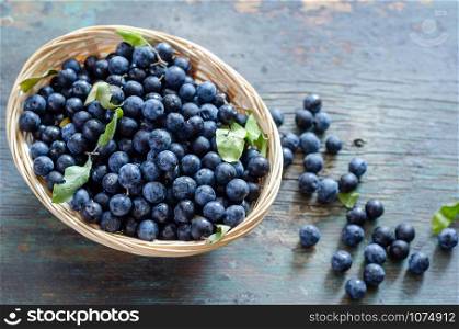 Blueberries with blueberries leaves in the wooden bowl on the table.