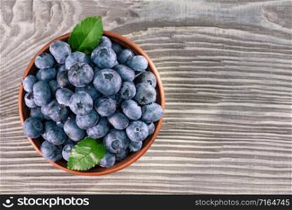 Blueberries with leaves in a brown clay bowl on a wooden background. View from above. Blueberries with leaves in clay bowl on wooden background