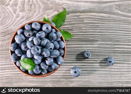 Blueberries with leaves in a clay bowl on a wooden table. View from above. Blueberries with leaves in clay bowl on wooden table
