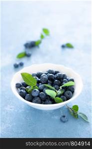 Blueberries with leaves in white bowl on blue background, top view