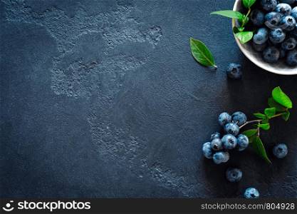 Blueberries with leaves on black background, top view