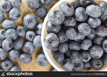 Blueberry berries on a table in a round white bowl, summertime, photo of ripe and tasty berries scattered on a wooden table and in a plate, closeup. Blueberry berries on a table