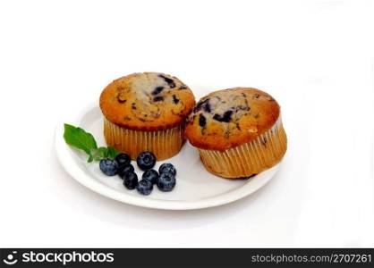 Blueberry muffins on a white plate with fresh berries on the side. Two Muffins
