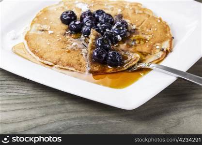 Blueberry pancakes with lot&rsquo;s of maple syrup on white plate with fork