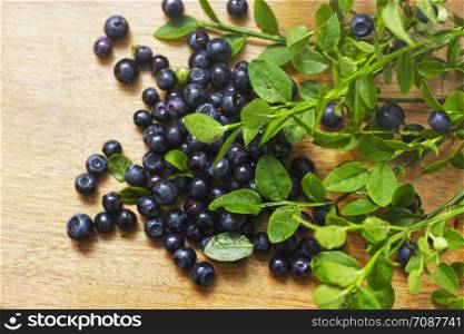 Blueberry. Ripe blueberries are scattered on a wooden table among the green leaves.
