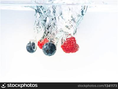 Blueberry&rsquo;s and raspberries splashing into crystal clear water with air bubbles
