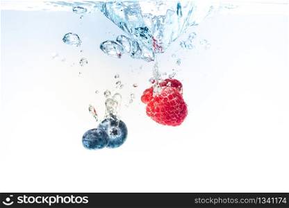 Blueberry&rsquo;s and raspberries splashing into crystal clear water with air bubbles