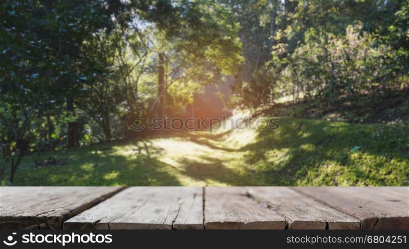 blur image of sunlight in morning on green grass in the park with selected focus empty wood table for display your product