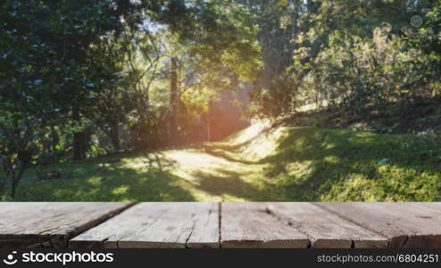 blur image of sunlight in morning on green grass in the park with selected focus empty wood table for display your product