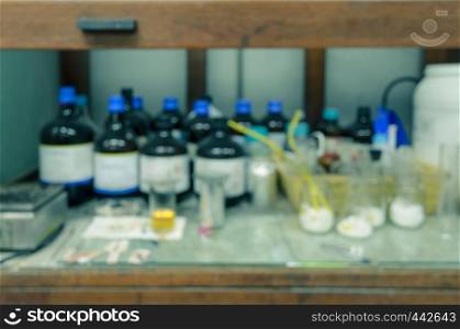 Blurred abstract background of old wooden chemical hood with reagent bottles in laboratory