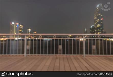 Blurred abstract background of wooden riverwalk with cityscape illuminated at night