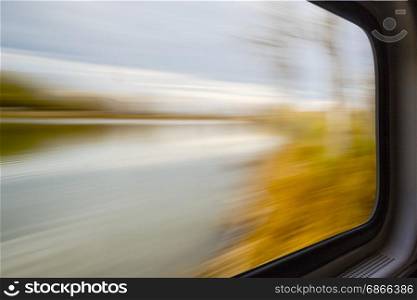 blurred abstract landscape of lake and forest seen from a train window in motion