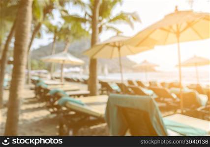 Blurred back view image of sun beds and umbrellas on tropical sandy beach with coconut tress