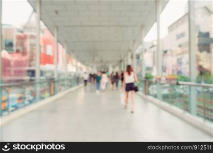 Blurred background image of people walking on skywalk in the city, surrounded by shopping mall and modern buildings. Bangkok, Thailand.