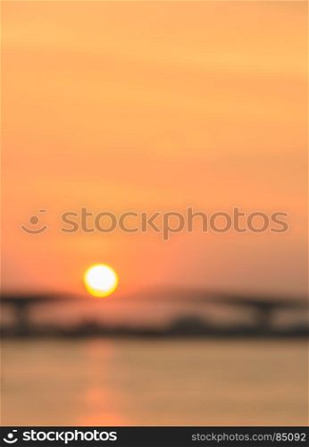 Blurred background of golden sunset sky with sun over the river bridge