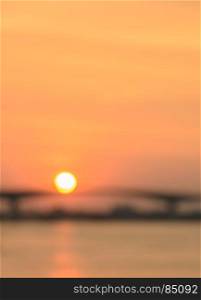 Blurred background of golden sunset sky with sun over the river bridge