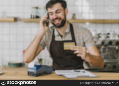 blurred barista with credit card speaking smartphone