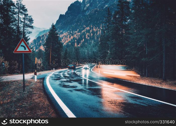Blurred cars in motion on the road in autumn forest in rain. Perfect asphalt mountain road in overcast rainy day. Roadway, pine trees in italian alps. Transportation. Highway in foggy woodland. Travel