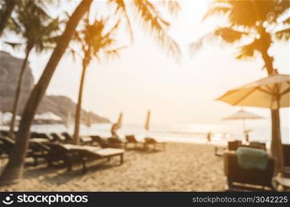Blurred image of sun beds and umbrellas on tropical sandy beach with coconut tress at sunset