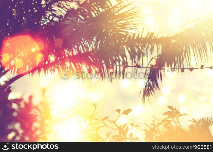 blurred light bokeh with coconut palm tree background on sunset, yellow string lights with bokeh decor in outdoor restaurant