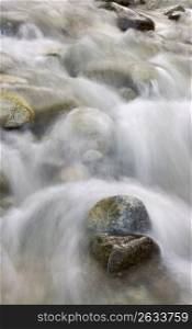 Blurred motion of stream water rushing over pebbles
