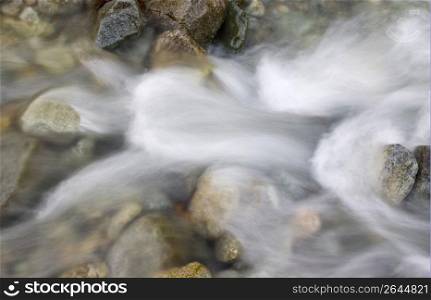 Blurred motion of stream water rushing over pebbles