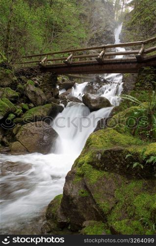 Blurred motion shot of stream and waterfalls in remote wooded area with footbridge