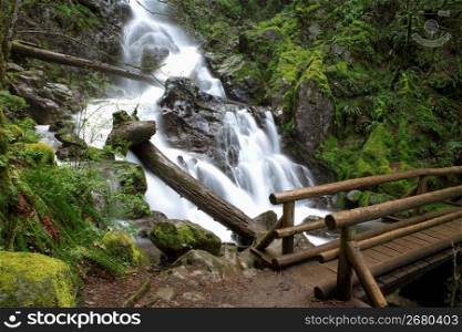 Blurred motion shot of stream and waterfalls in remote wooded area with footbridge in foreground