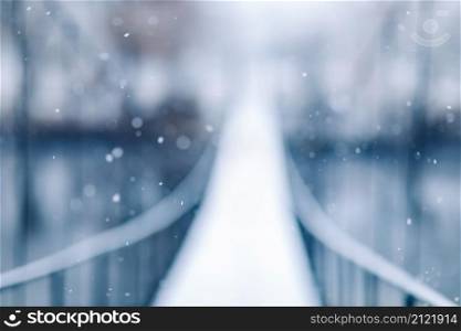blurred photo of Pedestrian suspension bridge made of steel and wood across the river, winter.. blurred photo of Pedestrian suspension bridge made of steel and wood across the river, winter
